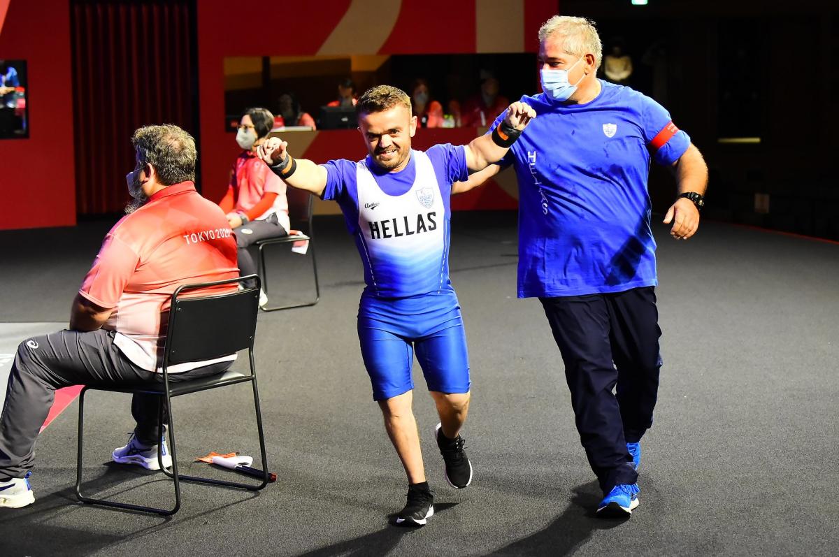 A man walking with his arms raised and a smile on his face while his coach taps him on the back.