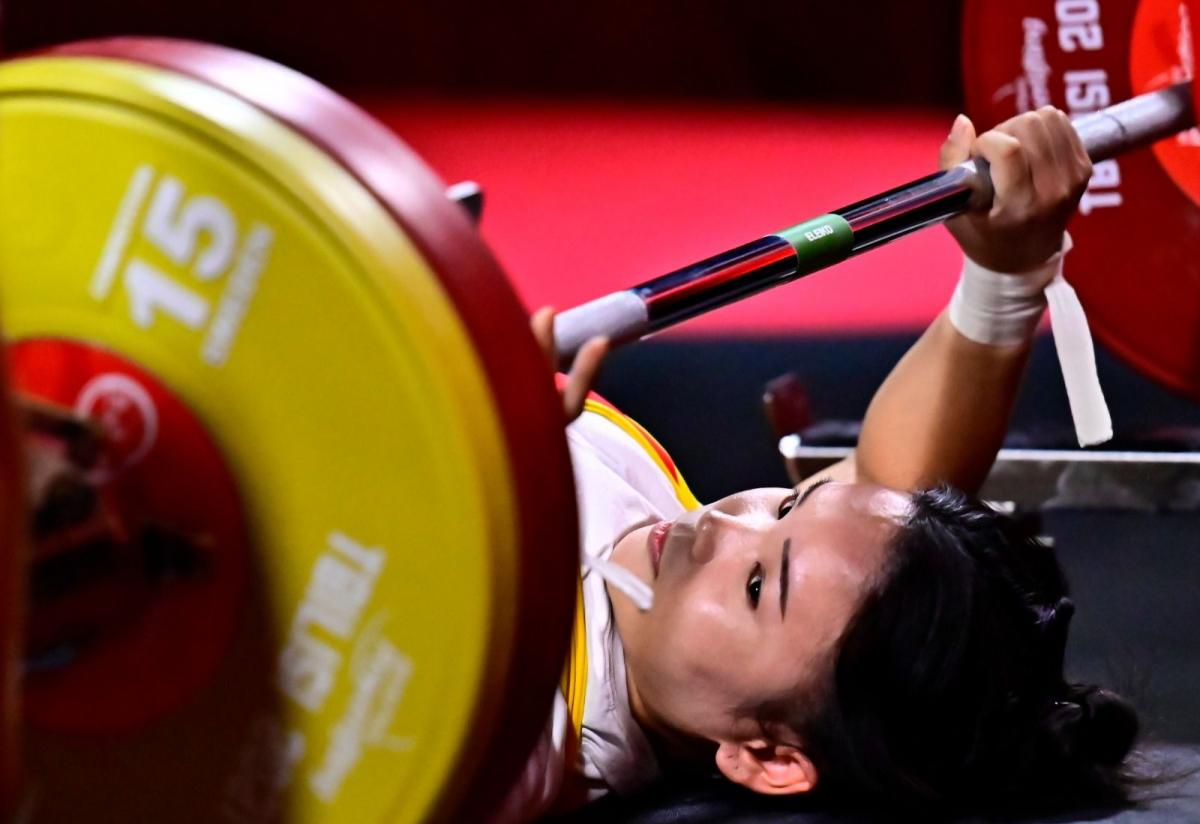 A woman on a bench press looking at the bar 