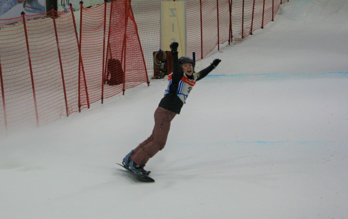 A female Para snowboarder stretching her arms in celebration in an indoor snow slope