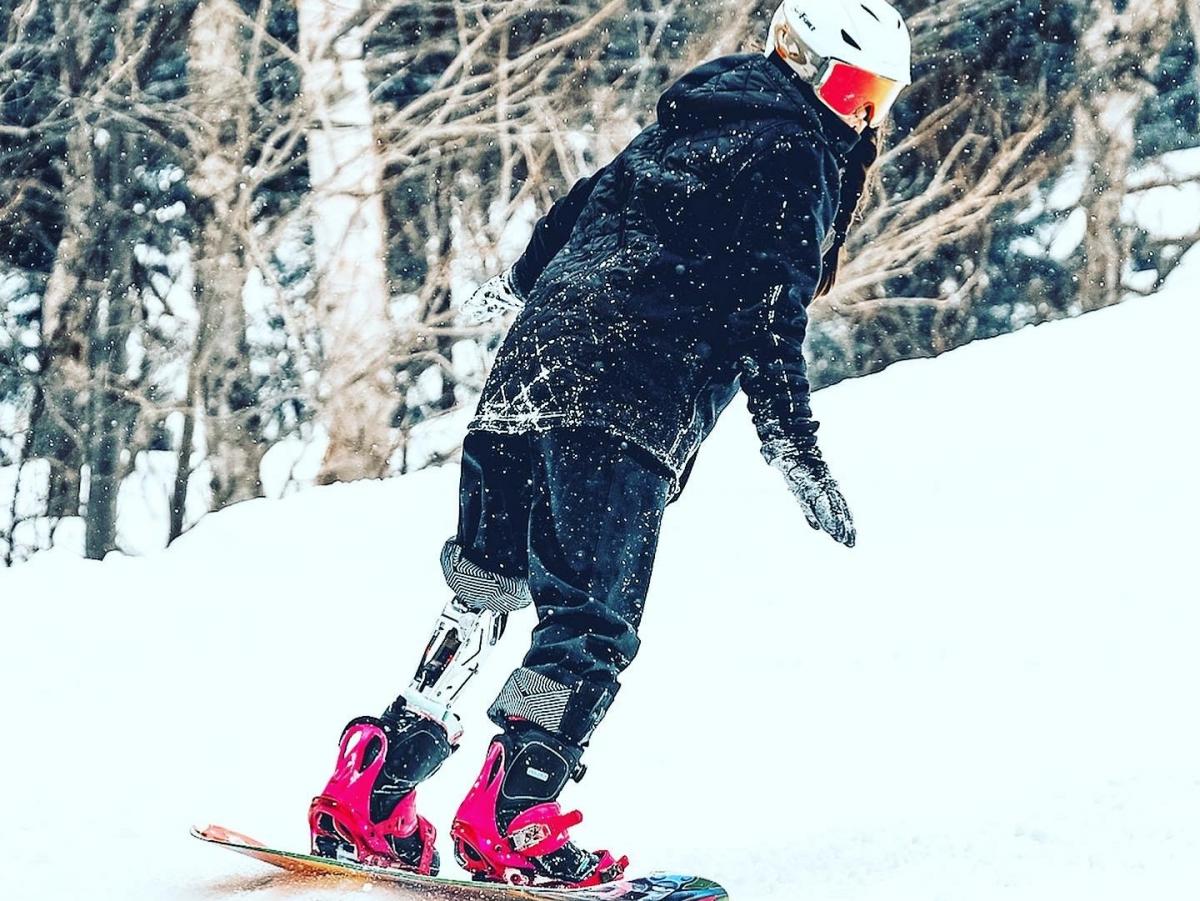 A female Para snowboarder with a prosthetic leg riding in the snow