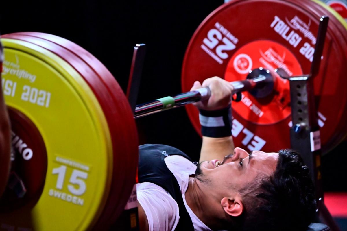 A young man lifting a bar in a Para powerlifting competition