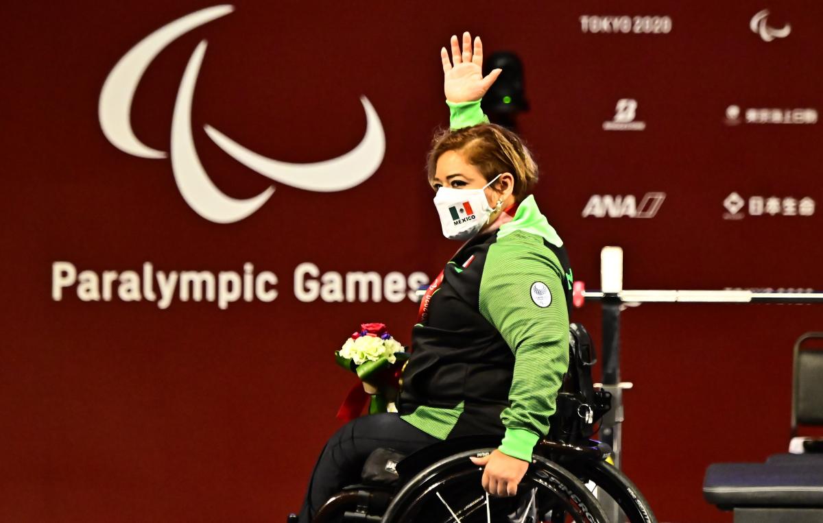 A woman in a wheelchair, raising her right hand high in celebration on the podium.