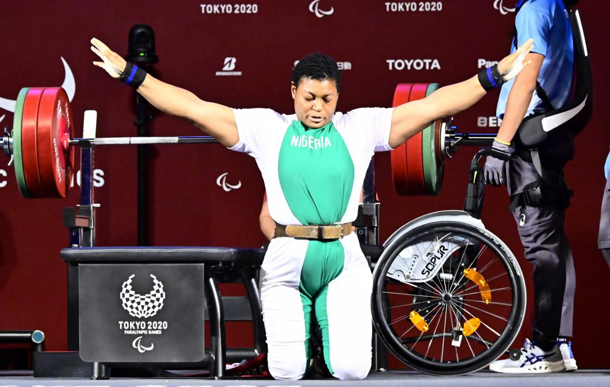 A woman on her knees in front of the bench celebrating with open arms and her eyes closed.