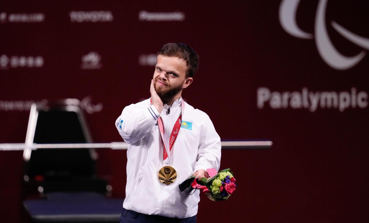 A man standing on the podium holding flowers in one hand and touching his face with the other hand