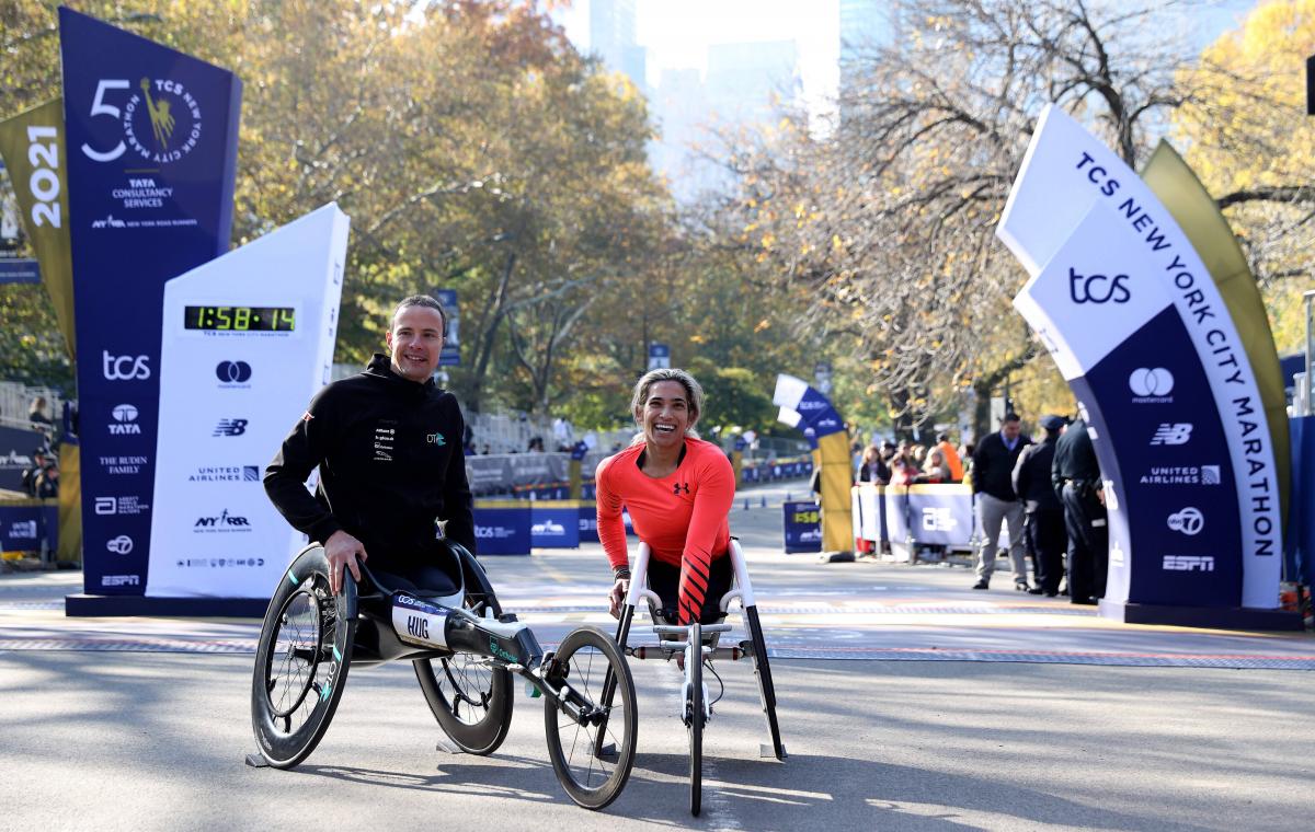 A man and a woman in wheelchair posing for a photo in front of the marathon finish line