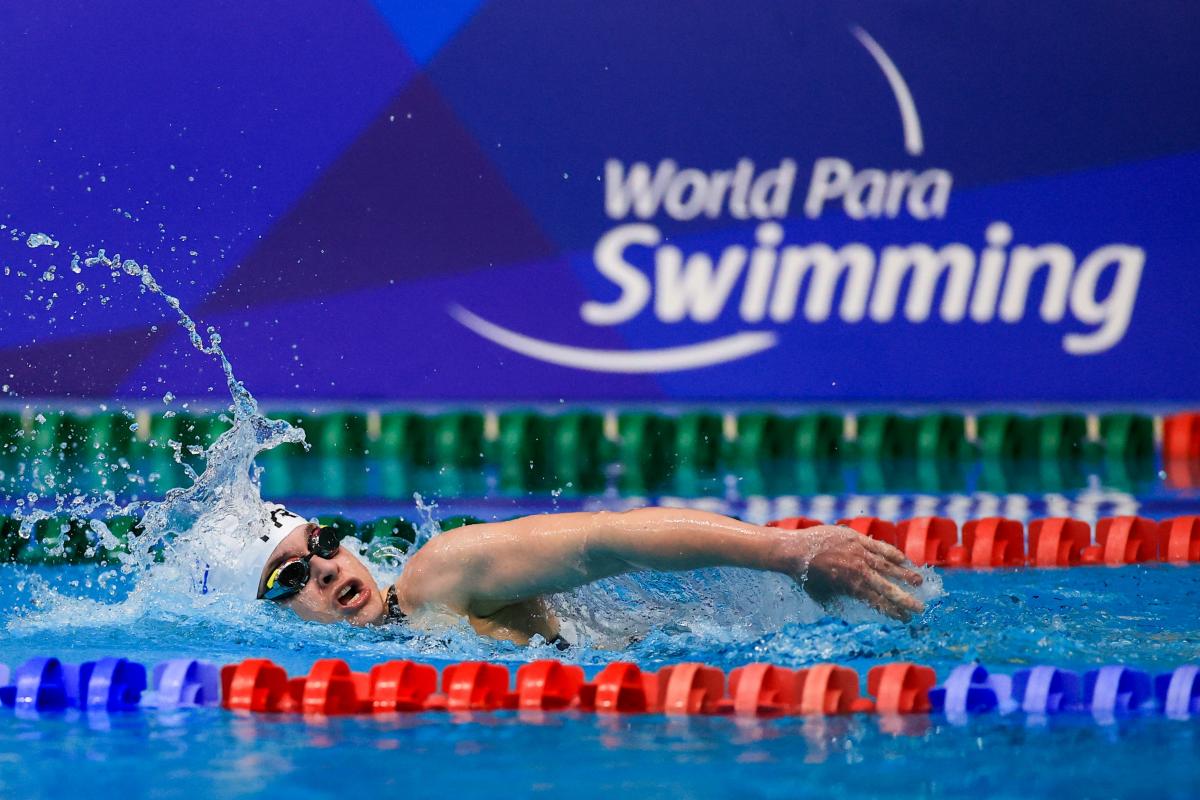 A female swimming in a pool with the logo of World Para Swimming on the background