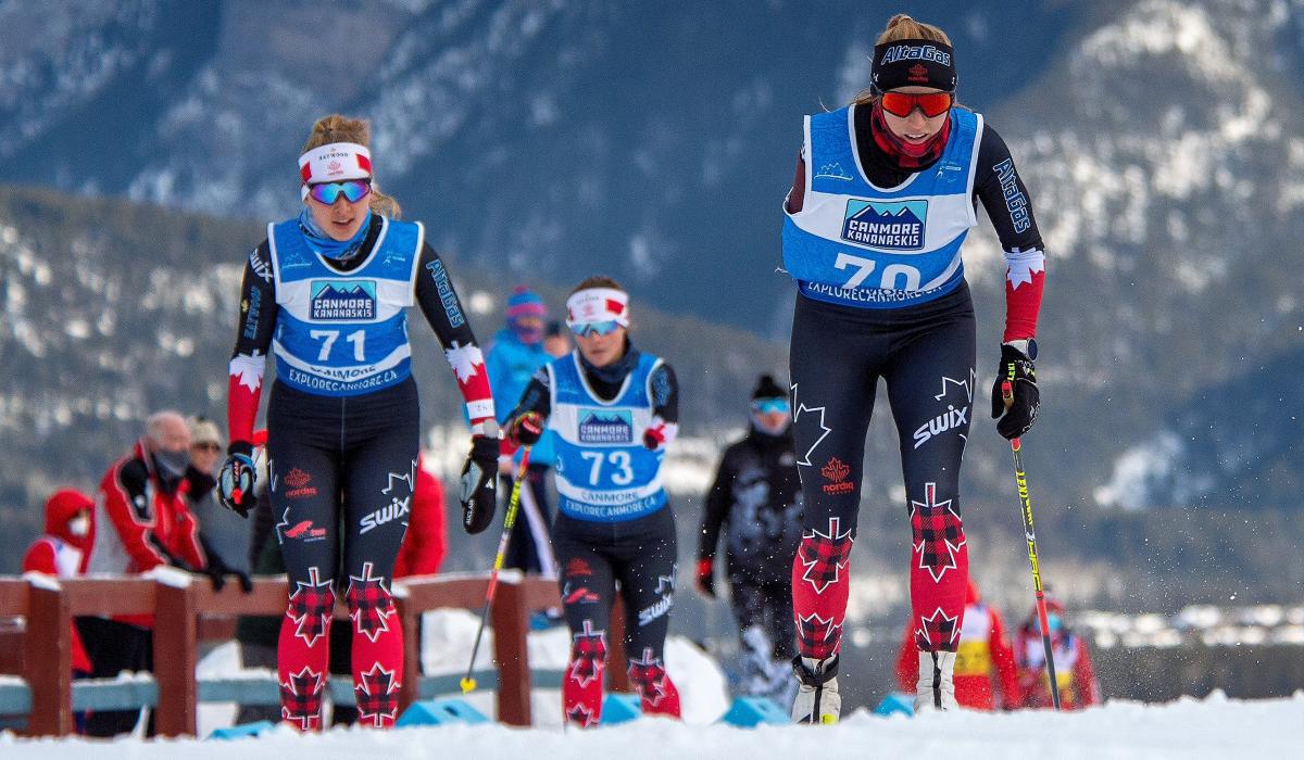 Three standing skiers climbing up the hill on a snowy road