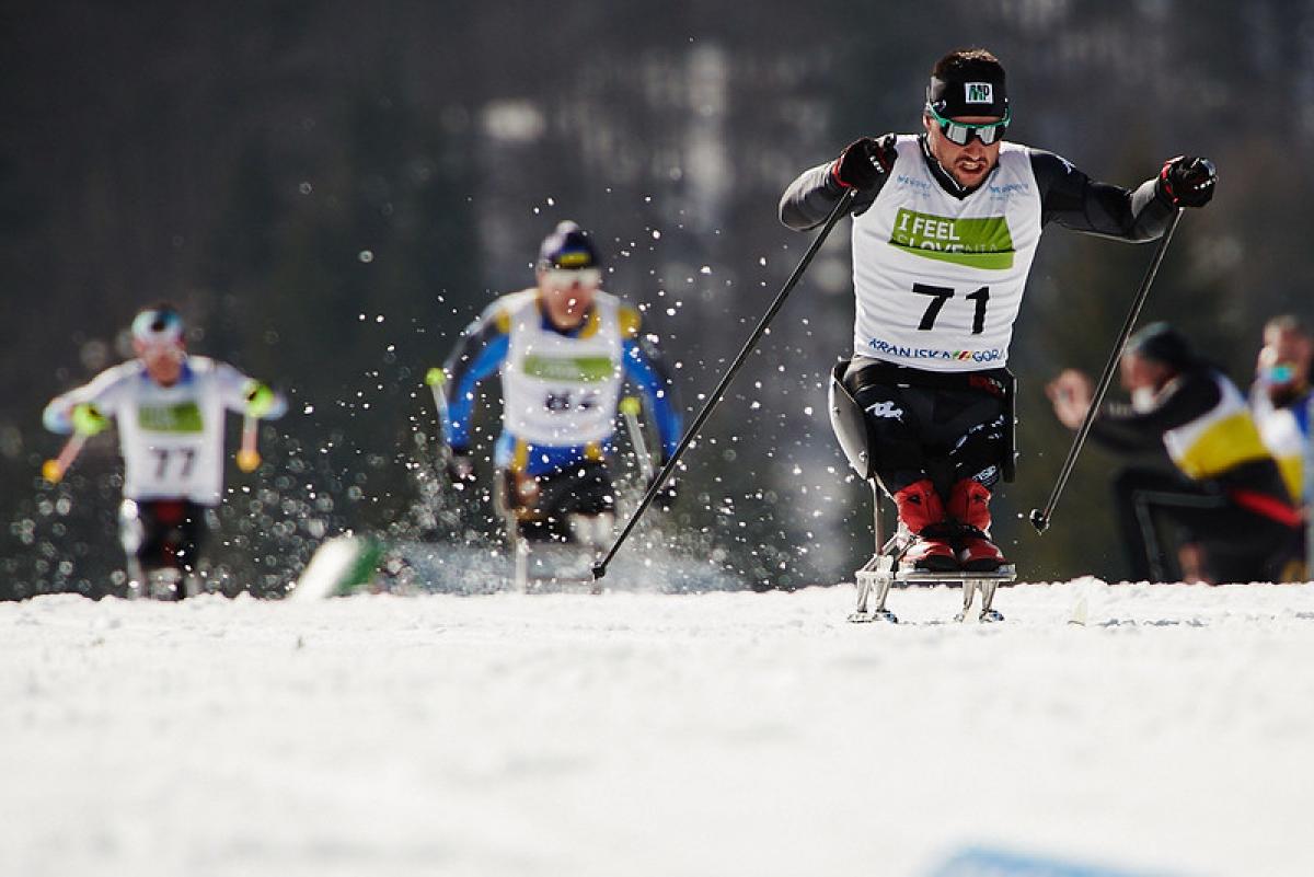 A male sit skier competing in cross-country ahead of two competitors