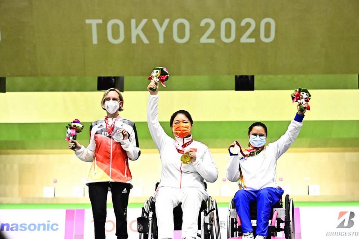 A woman standing next to two female wheelchair users on a podium at Tokyo 2020