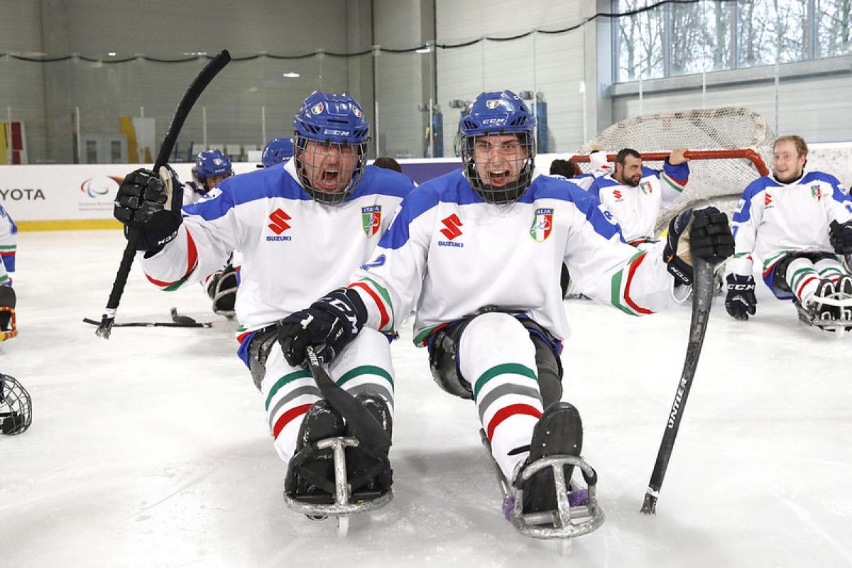 Two Italian Para ice hockey players celebrating with their team in the background in an ice rink