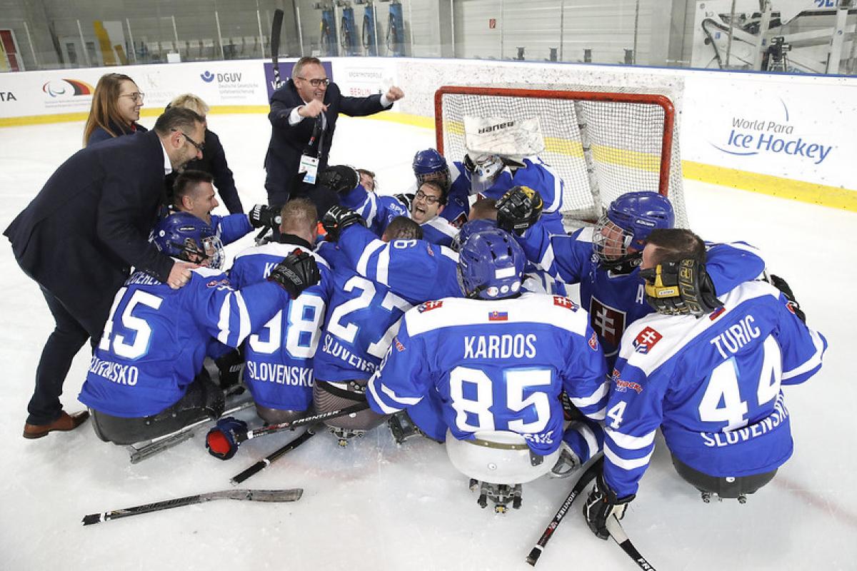 A group of Slovakian Para ice hockey players celebrating on an ice rink with four standing people