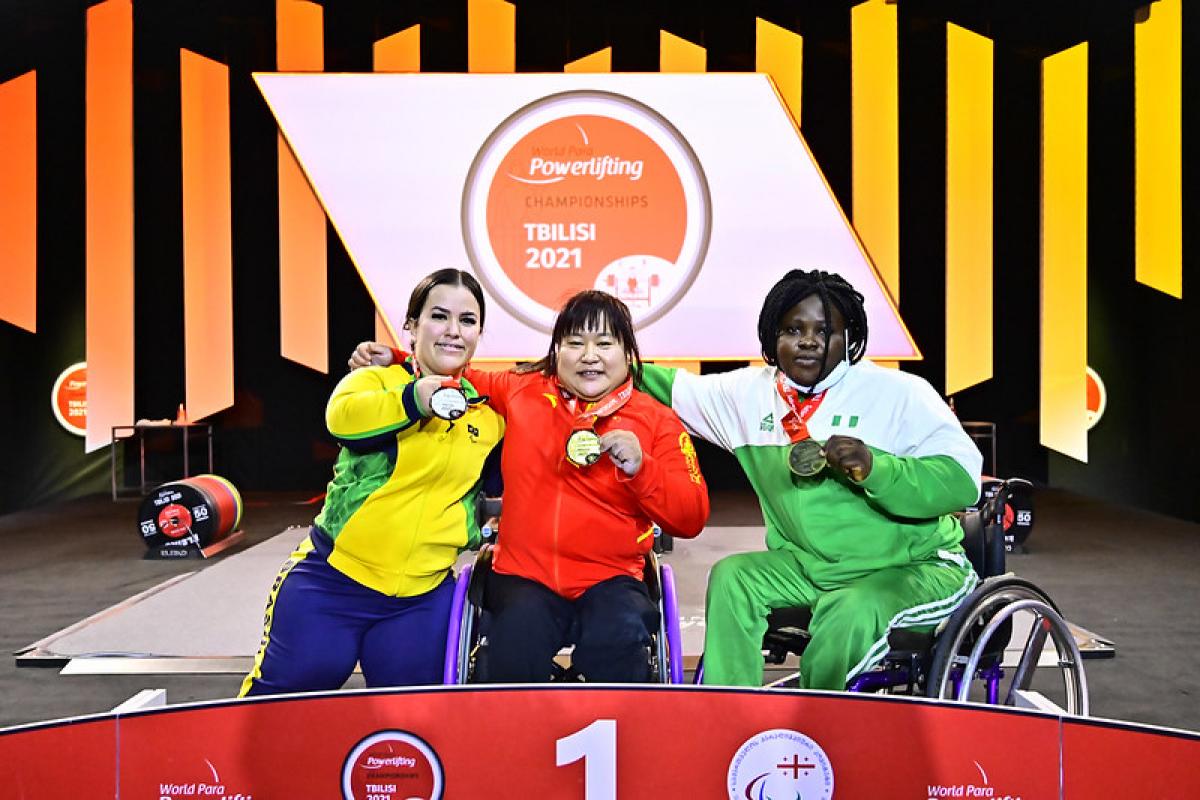 Three women on a podium showing their medals