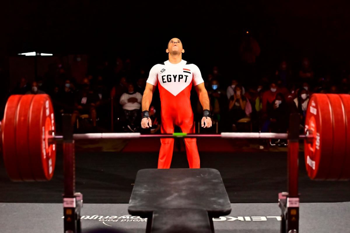 A man  looking up and standing in front of a bench press in a Para powerlifting