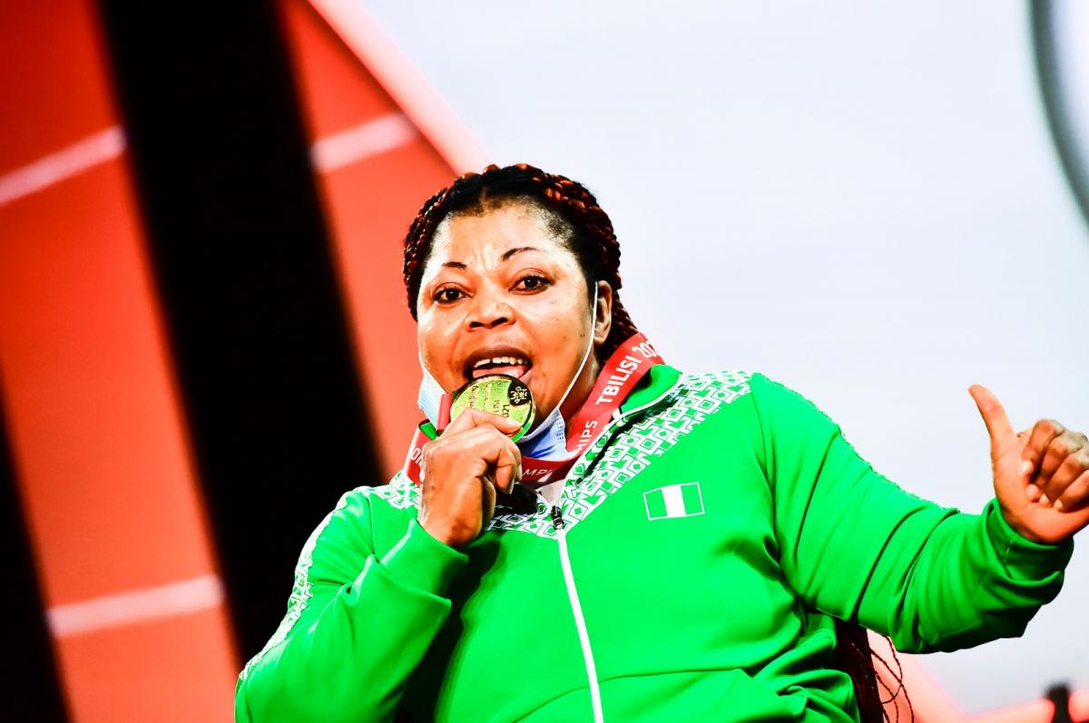 A woman in green uniform biting her gold medal