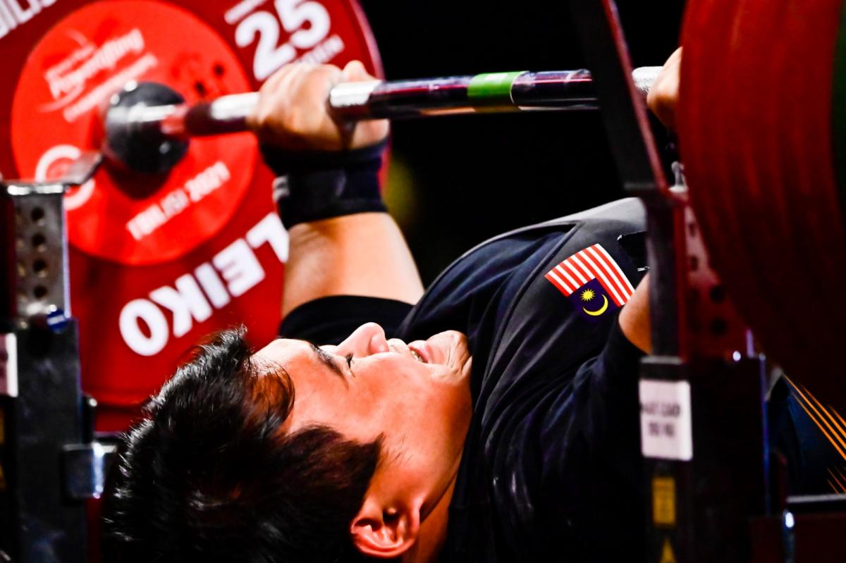 A man with an uniform with the flag of Malaysian pushing the bar on a bench press