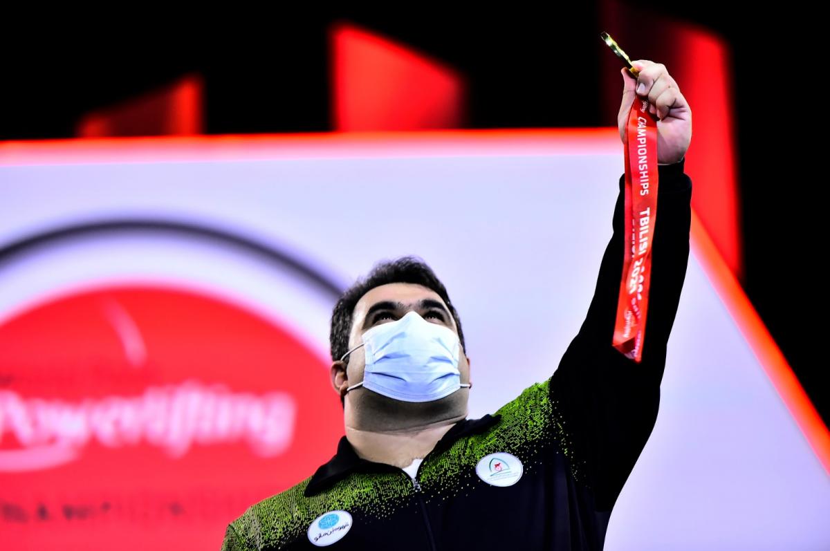 A man holding a gold medal and looking at the sky 