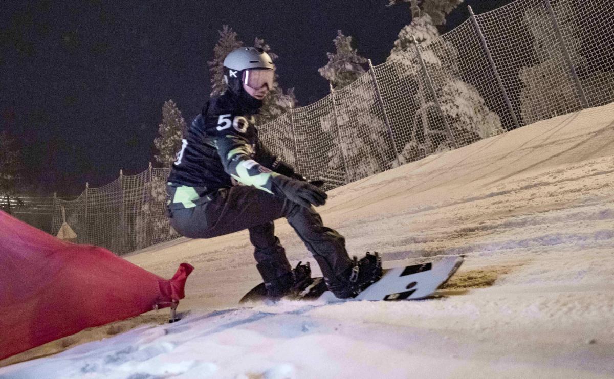 An athlete snowboarding during the night with goggles and helmet.