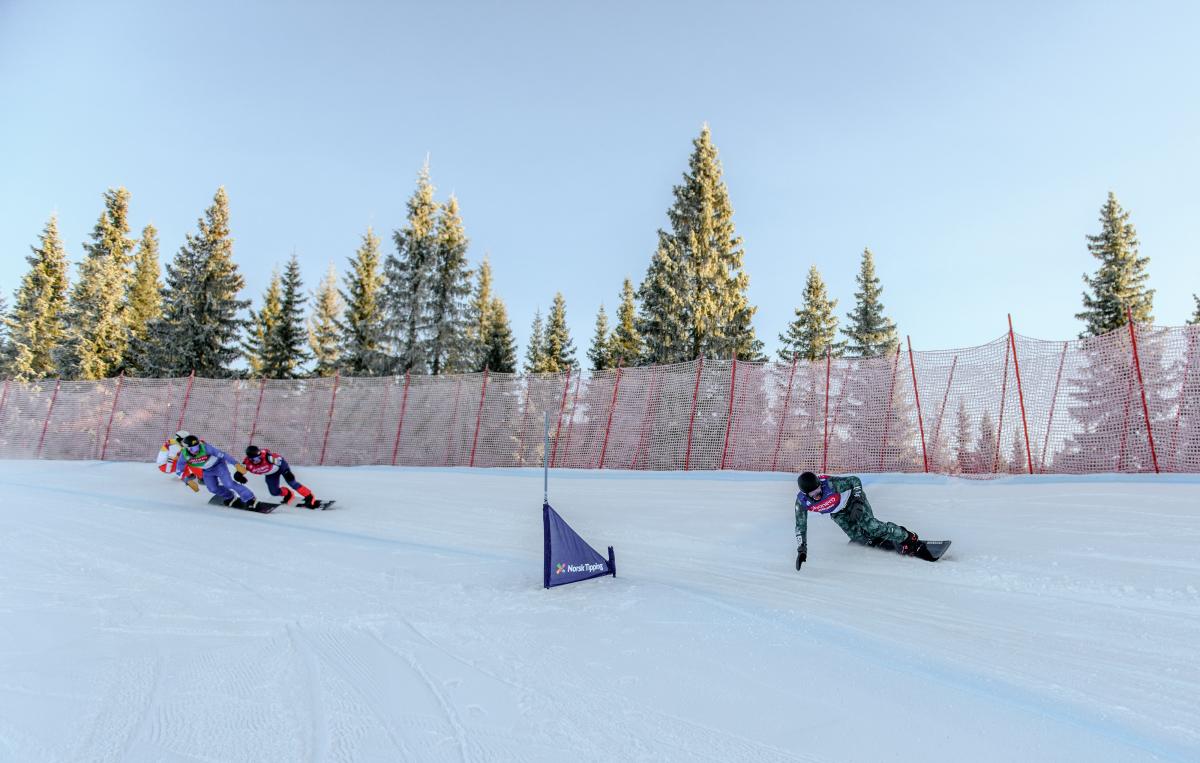 A male snowboarder ahead of three competitors in a snowboard cross