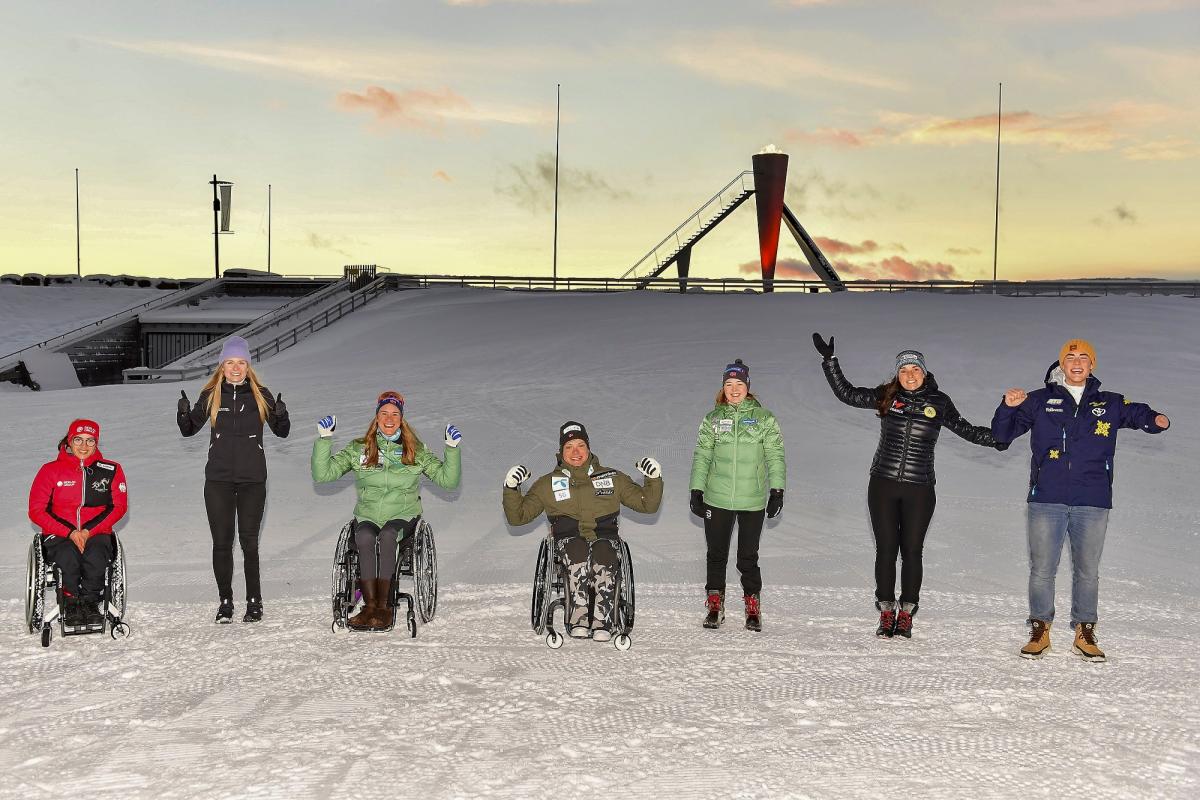 A group of three persons in wheelchairs and four standing persons on the snow