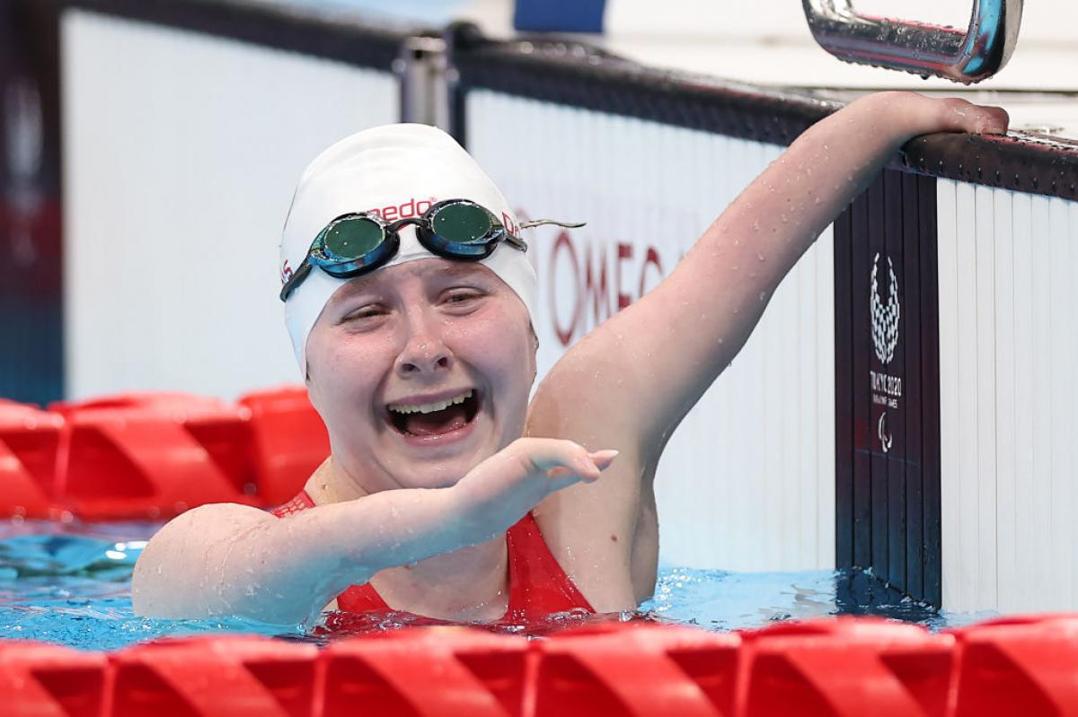A Para swimmer hanging onto the edge of the pool with a smile on her face