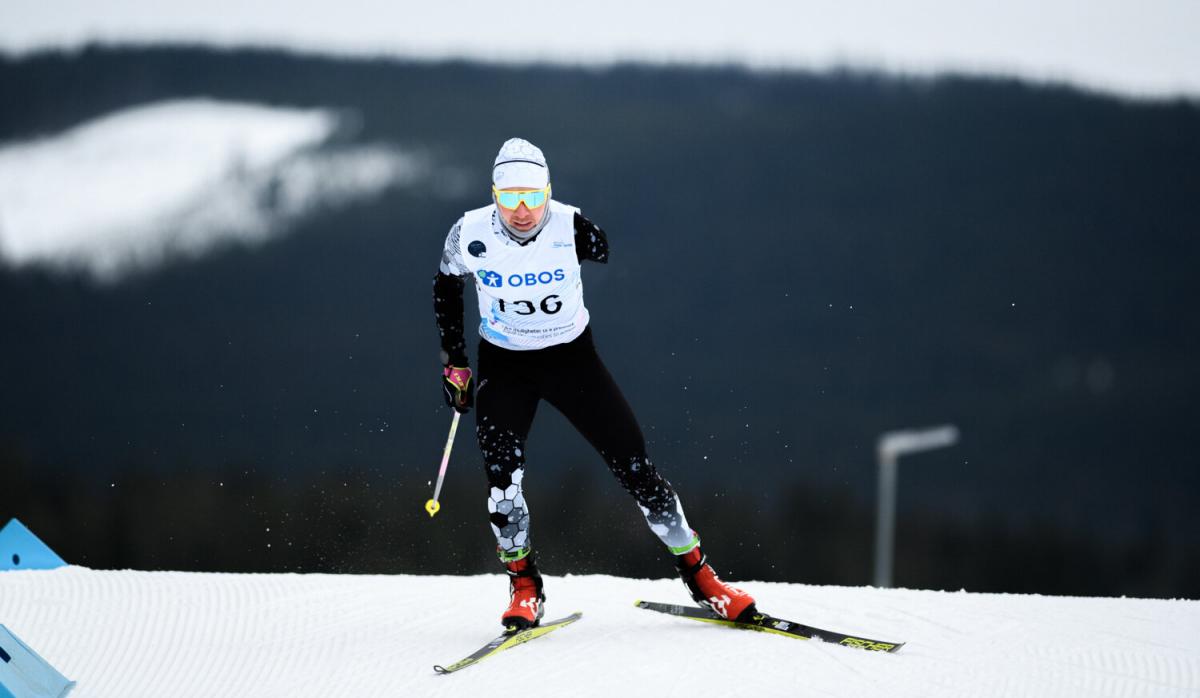 A man with two ski's and one stick in his right hand goes downhill on the snow circuit