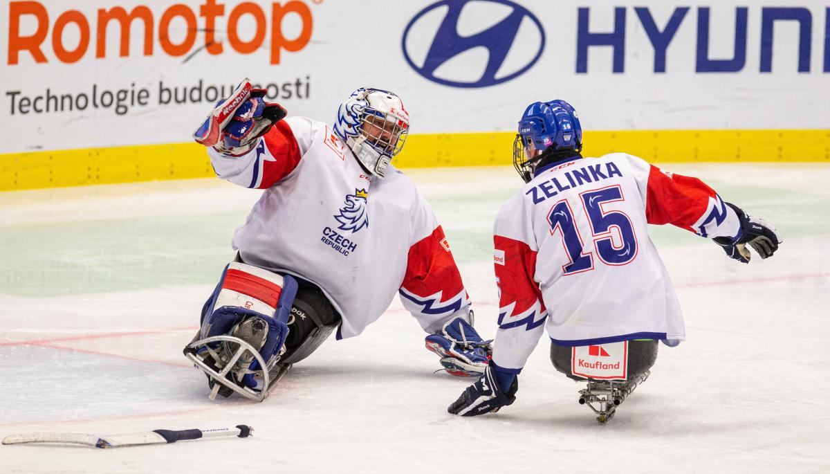 A goalie and a player sliding towards each other on the ice for a hug 