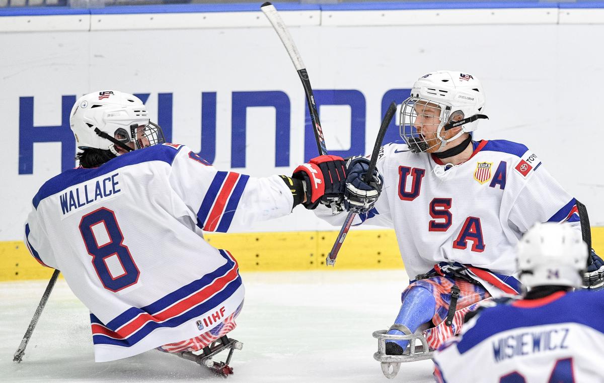 Two Para ice hockey players celebrating with a fist bump on their sledges.