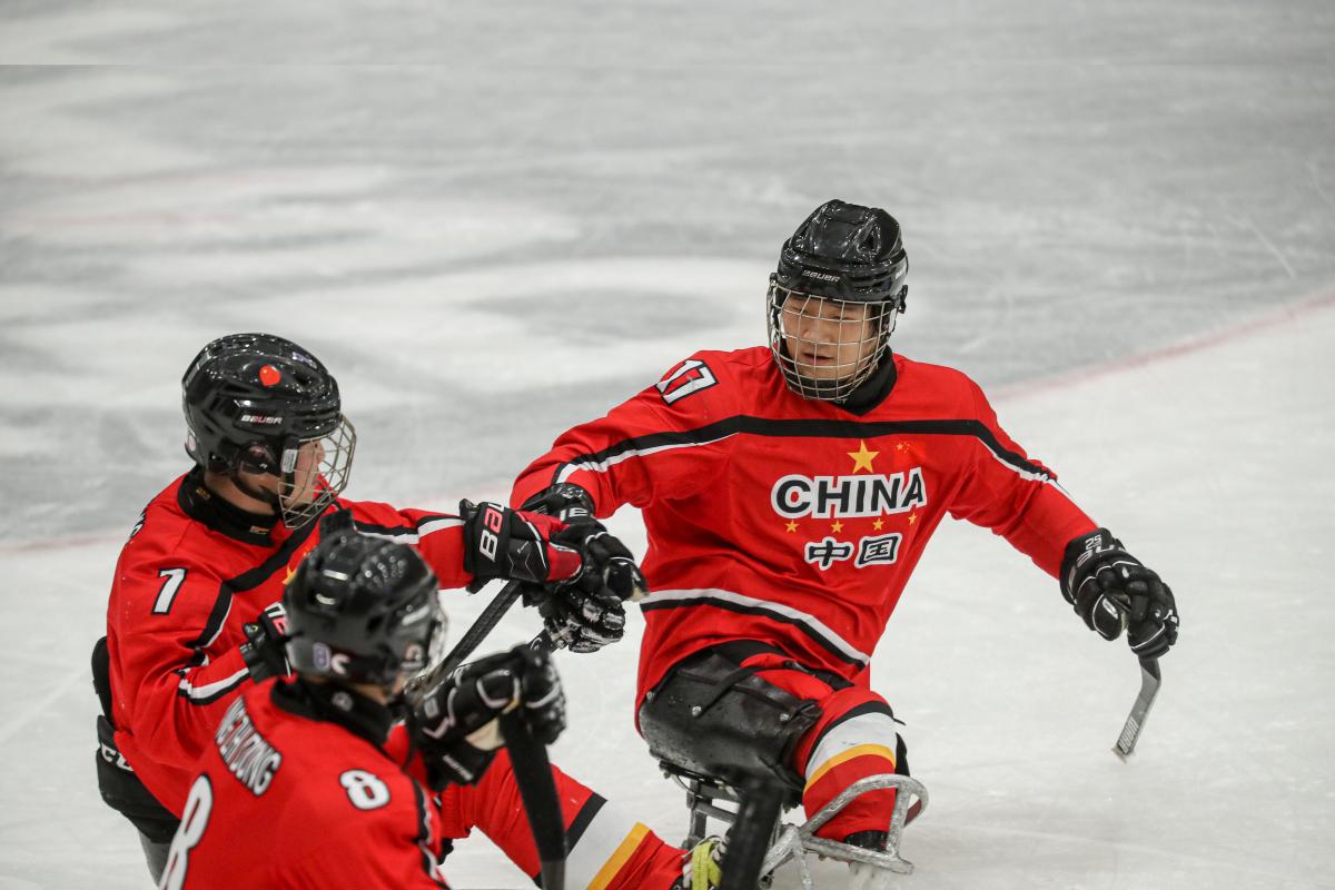 Three Para ice hockey players in red jerseys celebrating with fist bumps.