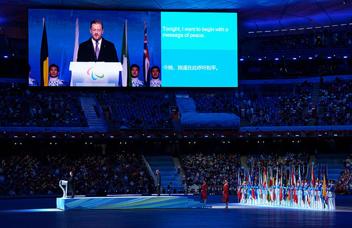 Andrew Parsons is pictured on a large screen at the Opening Ceremony of Beijing 2022 alongside a sentence of his speech which reads: 'tonight I want to begin with a message of peace'