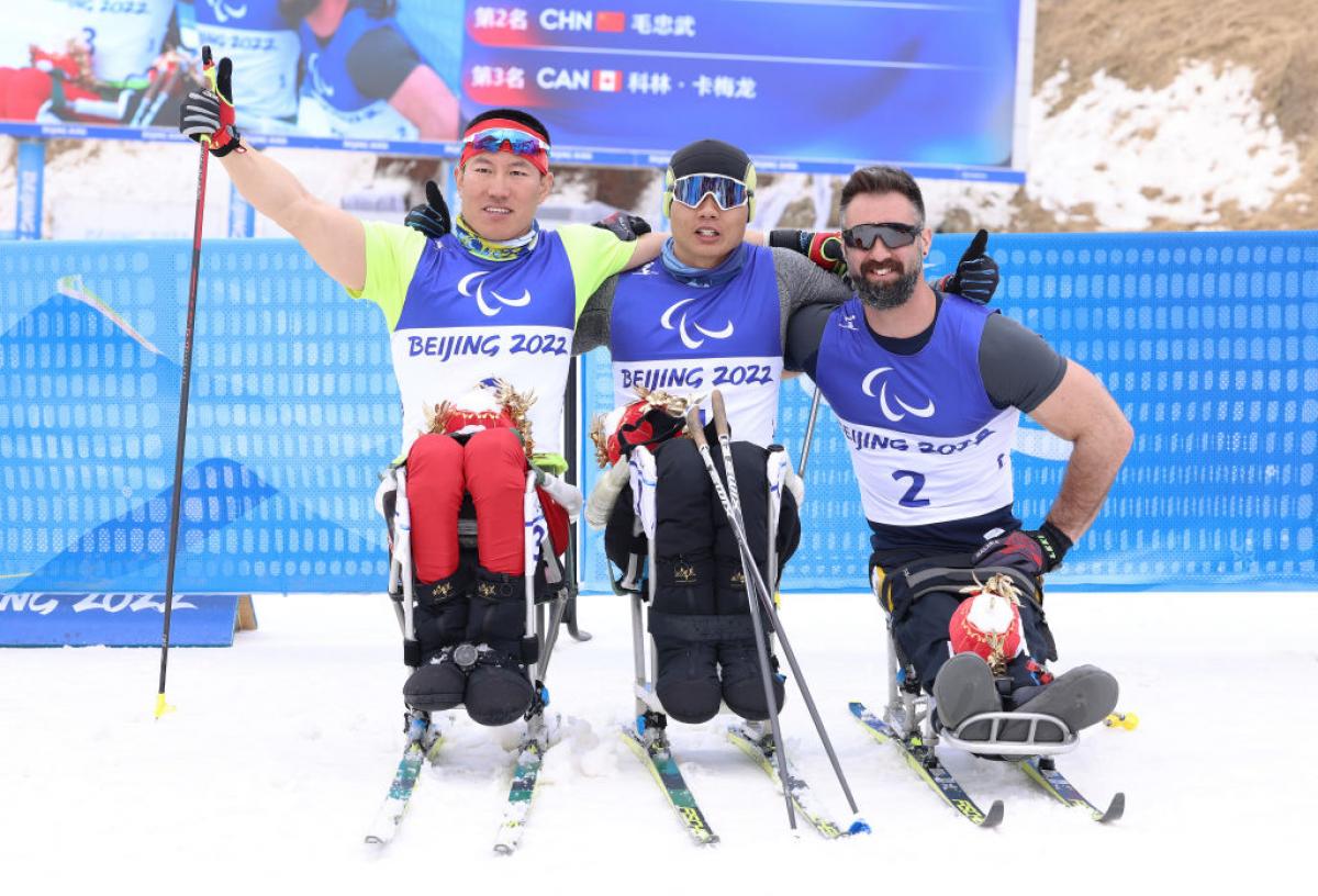 Gold medallist Zheng Peng of China (C), countrymate silver medallist Mao Zhongwu (L) and bronze medallist Collin Cameron of Canada (R) pose during Men's Sprint Sitting Final flower ceremony in the Beijing 2022 Paralympics Winter Games at Zhangjiakou National Biathlon Centre.