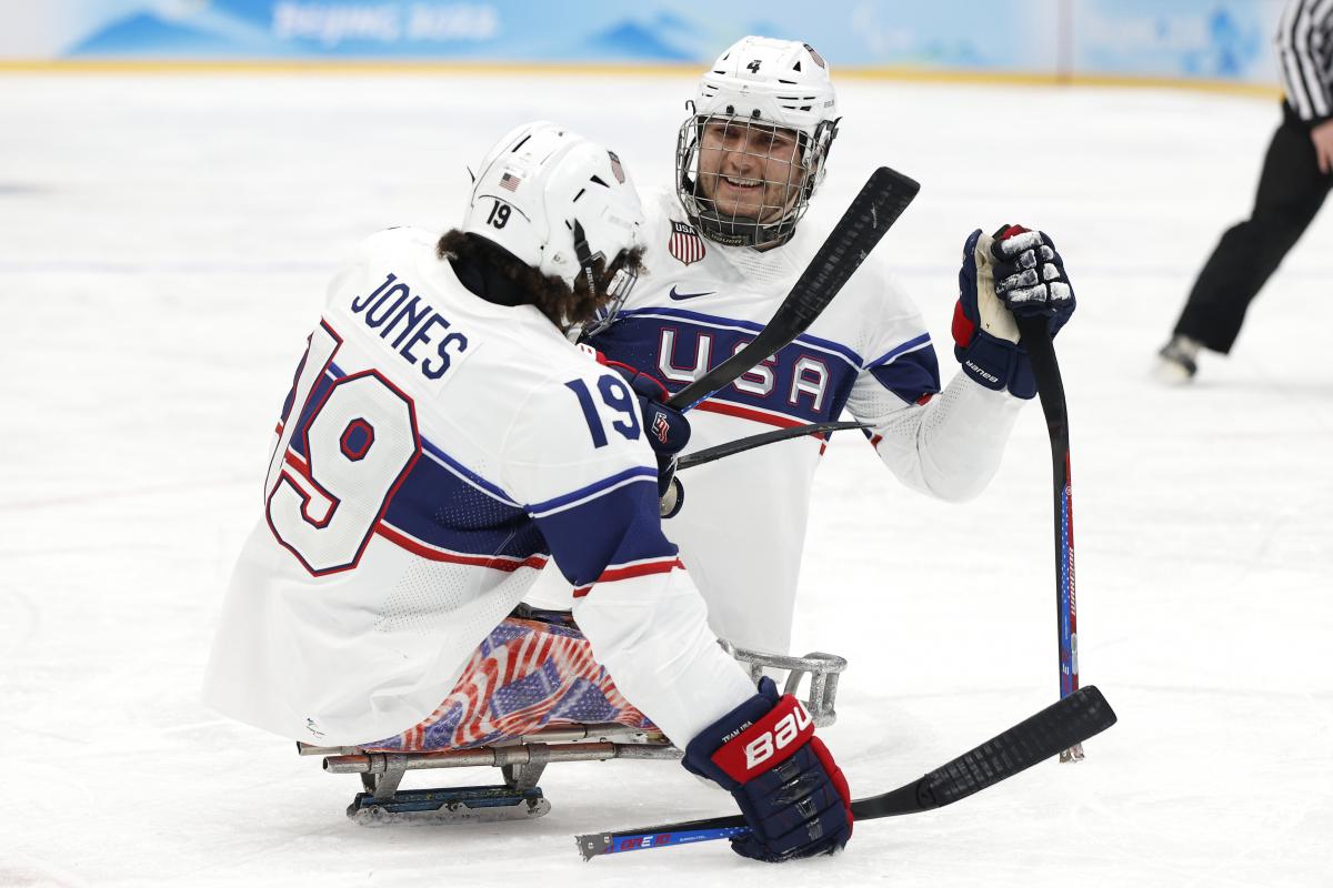 Two Para ice hockey players smiling to each other while on mono sleds.