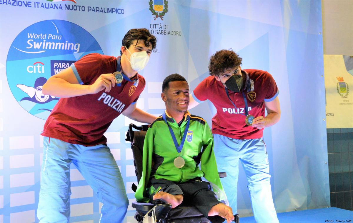 A man in a wheelchair in a medal ceremony with two standing men by his side