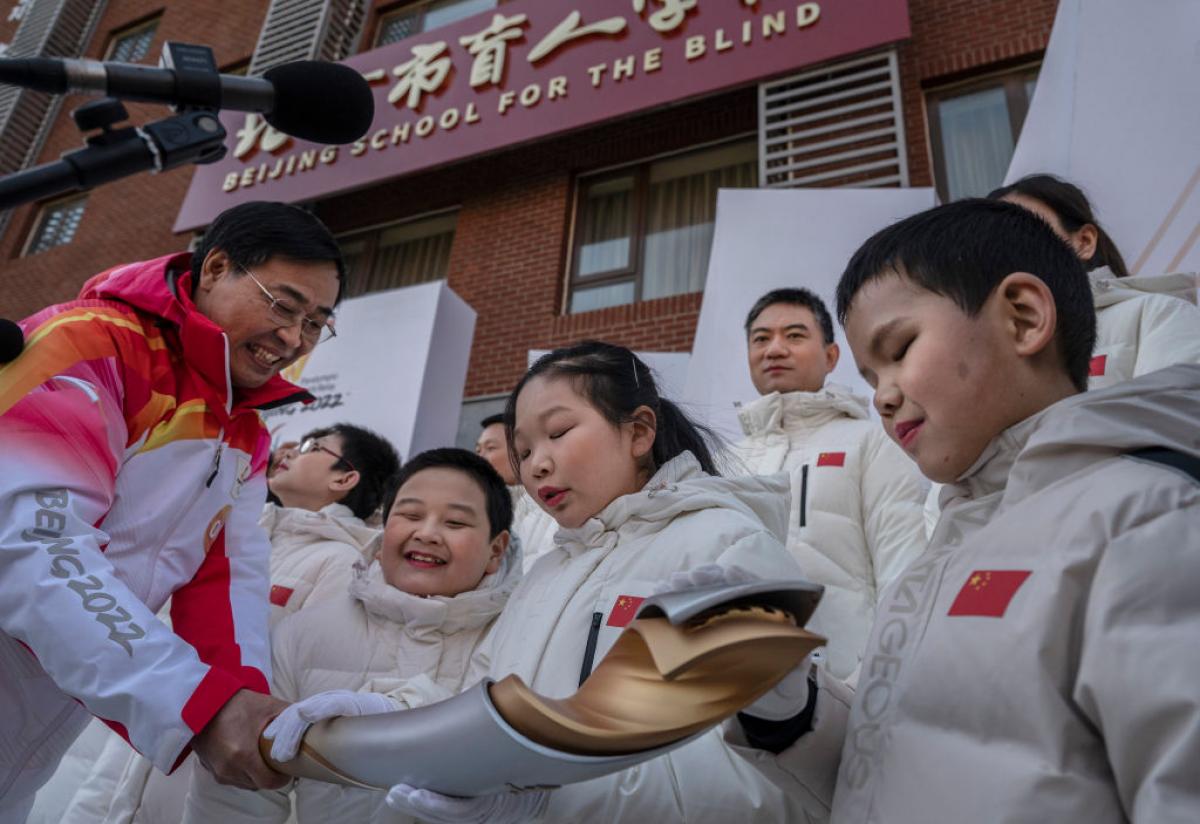 Students and choir members from the Beijing School for Blind feel and touch the torch as torchbearer Dr. Yao Yufeng (L) holds it out after the start of the Beijing 2022 Winter Paralympics Torch Relay. 
