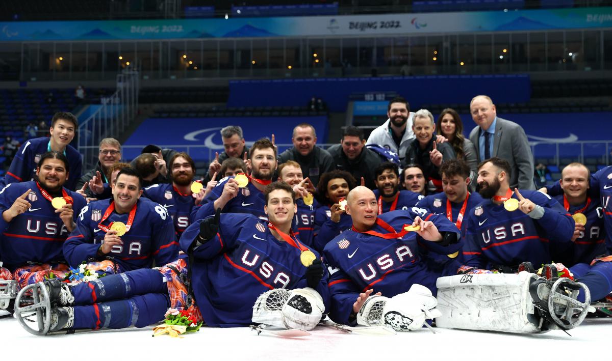 Team USA Para ice hockey players in full gear without helmets posing for a photo with gold medals.