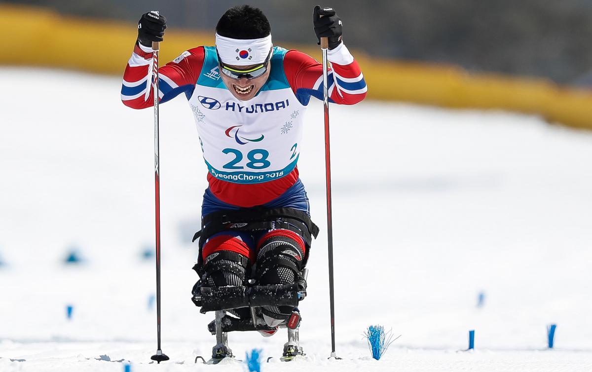 A man on sit ski's pushes himself towards the finish line with two sticks, one in each hand.