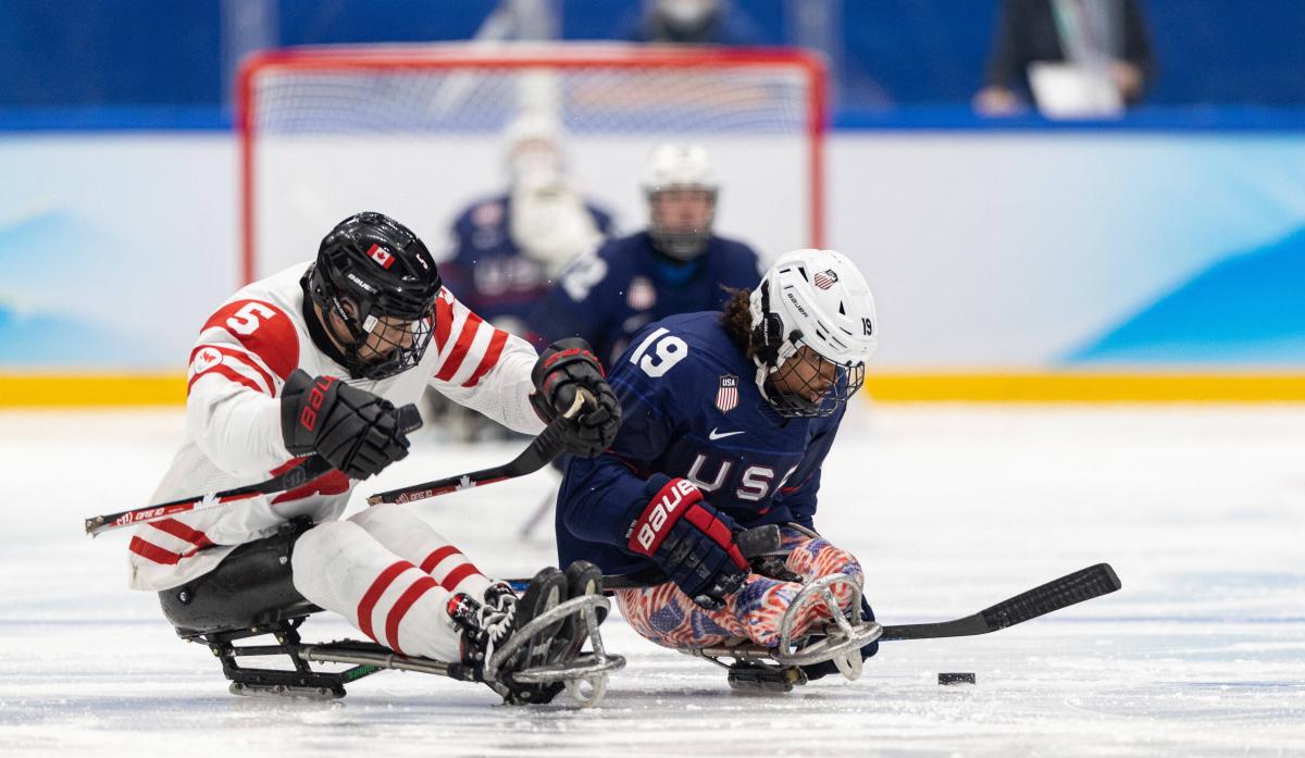 Two Para ice hockey players in full gear fighting for the possession.