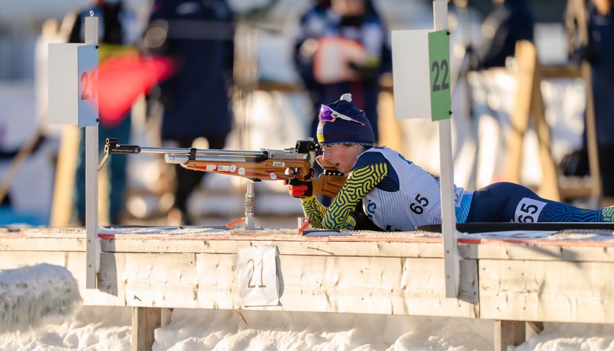 A female athlete lying on the floor aiming with the rival in her hands.