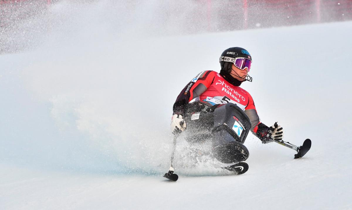 A man in a sit ski sliding into the snow.