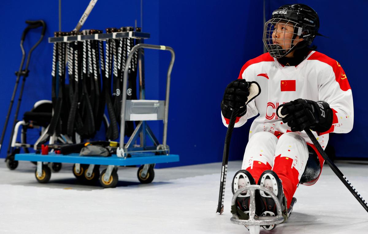 A woman sitting in a sled with a full Para ice hockey gear on her.