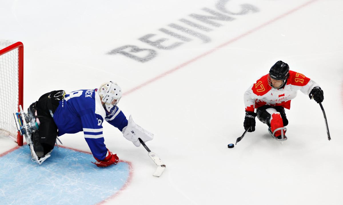 A Para ice hockey player moves past the goalie navigating the puck with a stick.