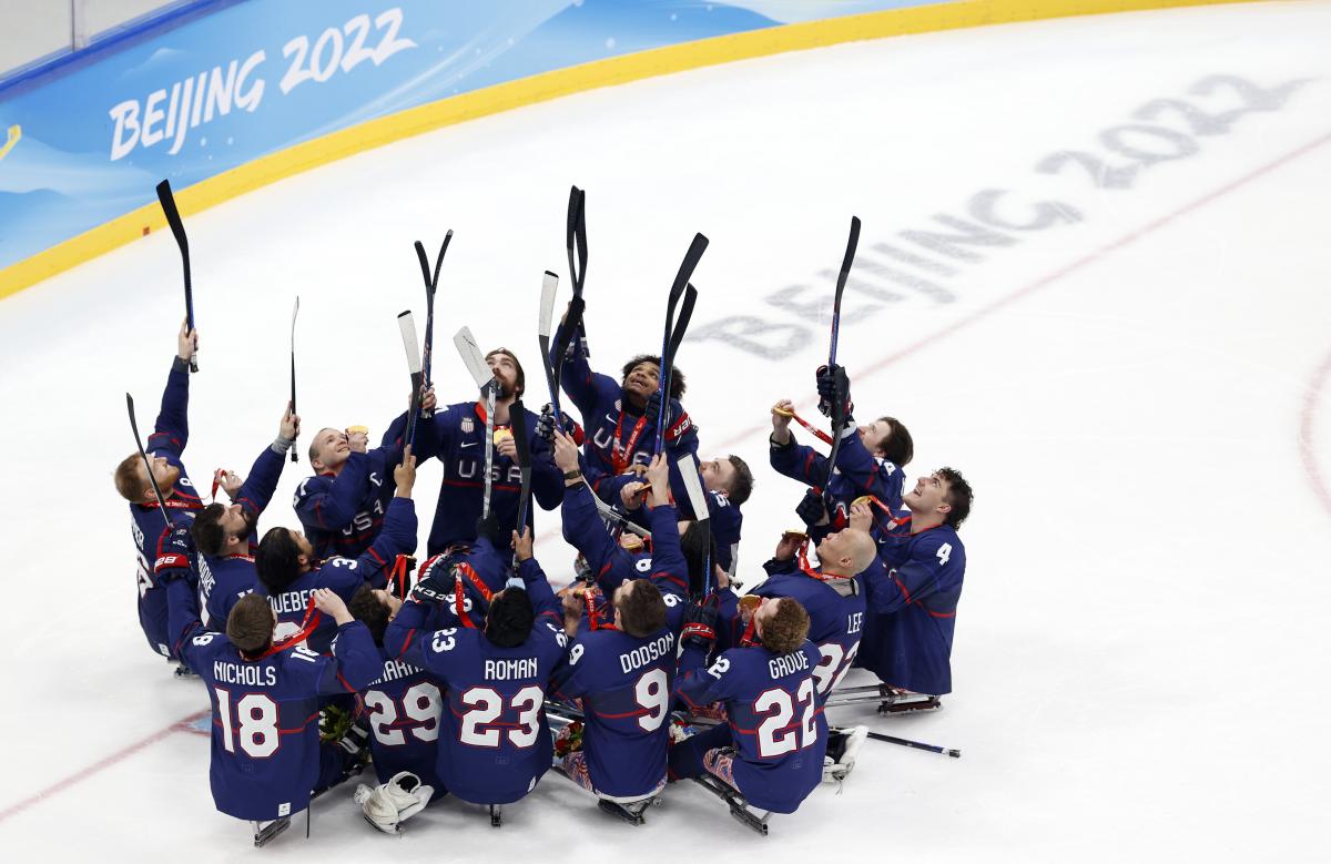 Team USA Para Ice Hockey players in full gear without helmets pointing with their sticks towards the top of the arena.