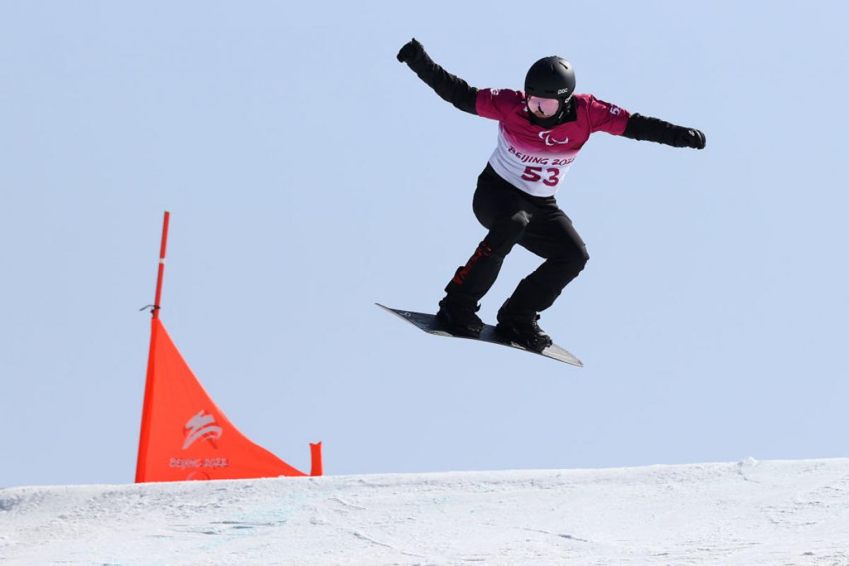 A man passing by a flag in a Para snowboard competition