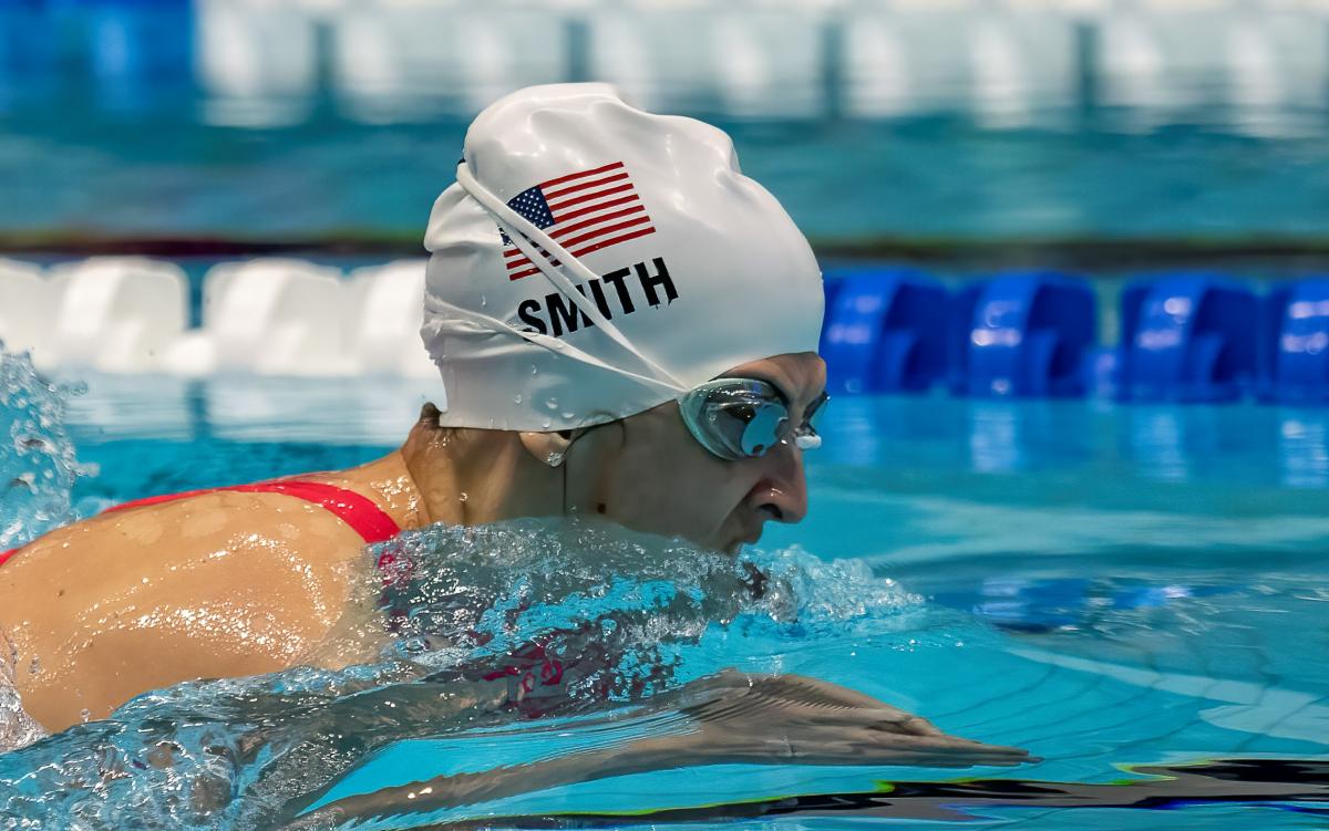 A female Para swimmer with a white cap swimming breastroke