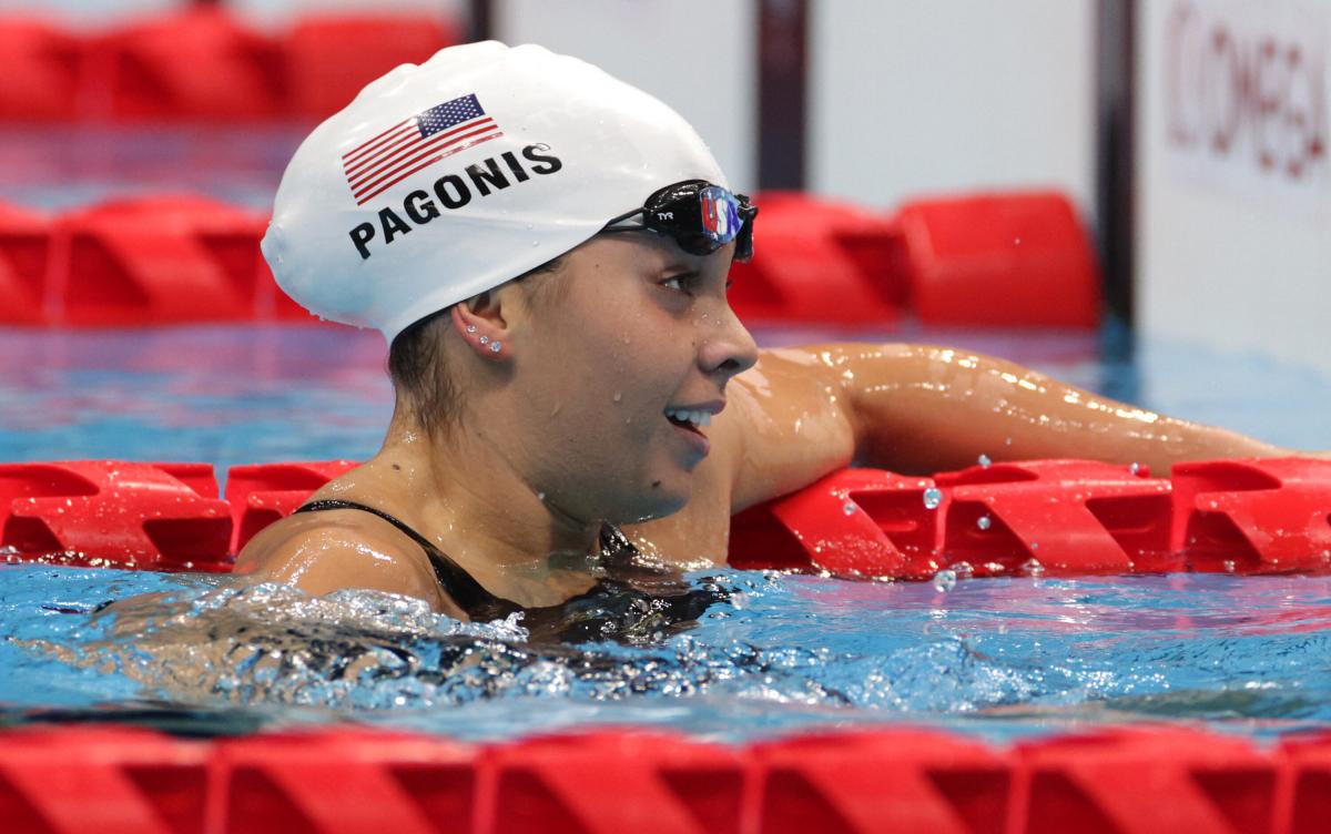 A female Para swimmer hanging on a rope with her left hand and the goggles off.