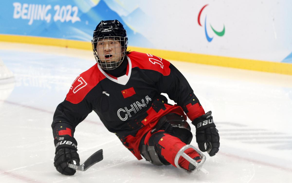 A Para ice hockey player in full gear slides on the ice.
