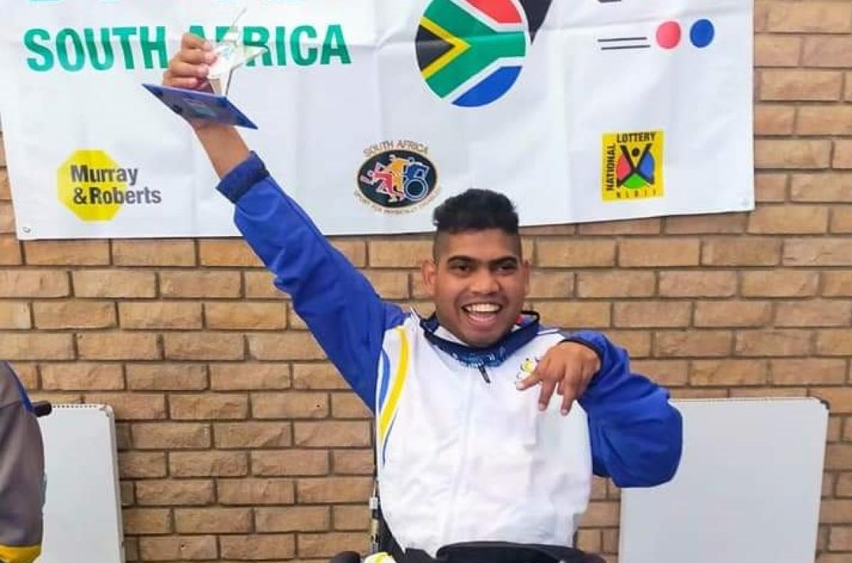 Liakath Aziz raises his arm in celebration while holding a trophy.