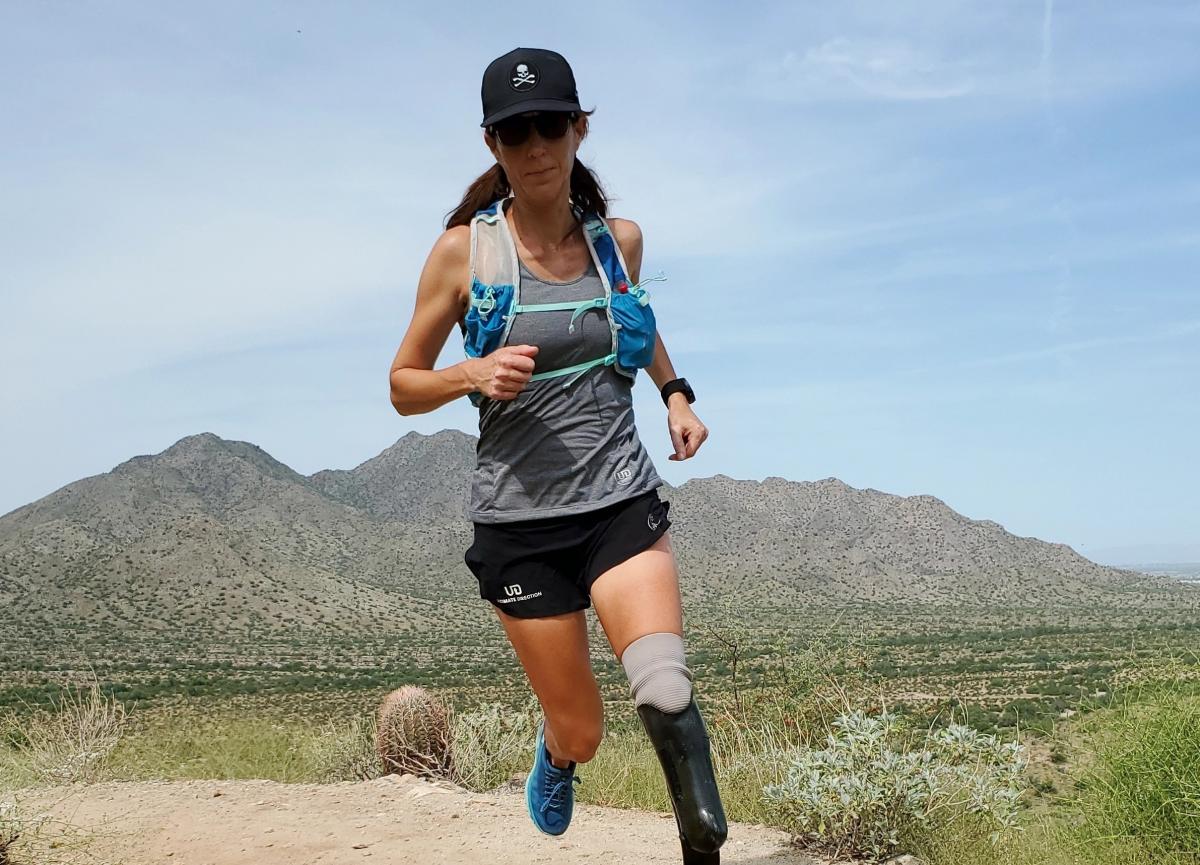 Jacky Hunt-Broersma runs along a sandy trail in Arizona with a mountain backdrop.