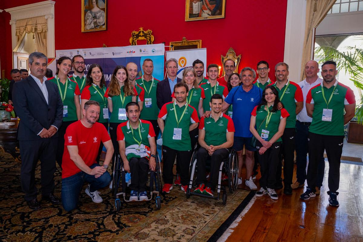 A group of people wearing the uniform of the Portuguese Para swimming team posing for a picture in a hall