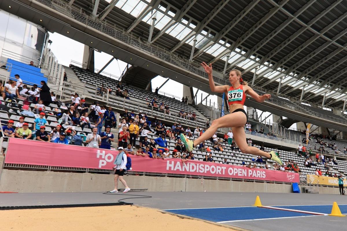 A woman competing in the long jump in front of the spectators in a stadium