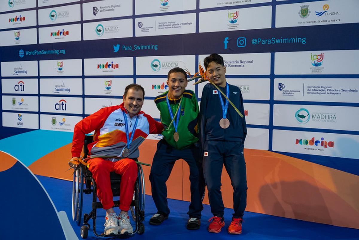 Three men with disabilities on a podium with their medals